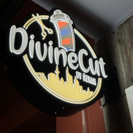Signage für Friseursalon "DivineCut" mit Silhouette einer Stadt im Hintergrund.