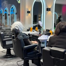 Friseur mit zwei Kunden, einer in einem modernen Stuhl, umgeben von stylischen Spiegeln.