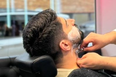 Mann beim Rasieren mit Schaum, Friseur bearbeitet seinen Bart in einem Friseursalon.